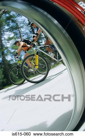 Stock Image - View of cyclists through wheel.. Fotosearch