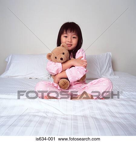 Stock Image - Young girl cuddling bear on bed. Fotosearch