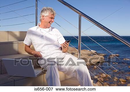 Man by the sea with laptop and mobile phone View Large Photo Image Stock Photo - Man by the sea with laptop and mobile phone . Fotosearch