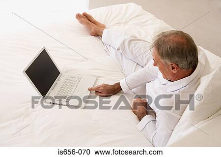Man using laptop on bed View Large Photo Image Stock Image - Man using laptop on bed. Fotosearch