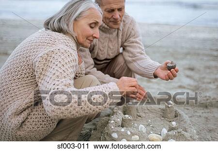 Stock Image - Senior couple making a sandcastle. Fotosearch