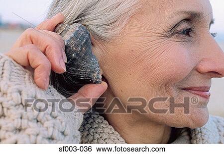 Senior woman holding a shell to her ear View Large Photo Image Stock Photograph - Senior woman holding a shell to her ear. Fotosearch