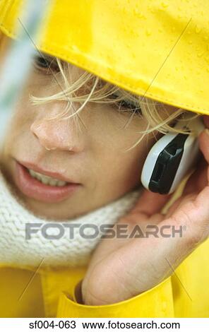 Stock Image - Close-up of woman in yellow raincoat using mobile phone. Fotosearch