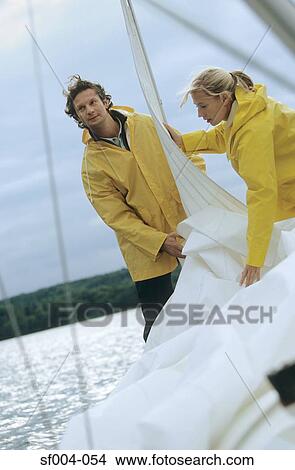 Couple taking down sail on boat View Large Photo Image Picture - Couple taking down sail on boat. Fotosearch