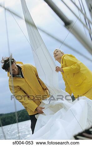 Couple taking down sail on boat View Large Photo Image Stock Image - Couple taking down sail on boat. Fotosearch