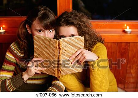 Two women peeking over a book View Large Photo Image Stock Photograph - Two women peeking over a book. Fotosearch