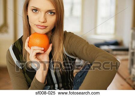 Stock Photography - Woman holding an orange under her chin. Fotosearch