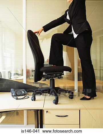 Stock Image - Businesswoman standing on an office chair. Fotosearch