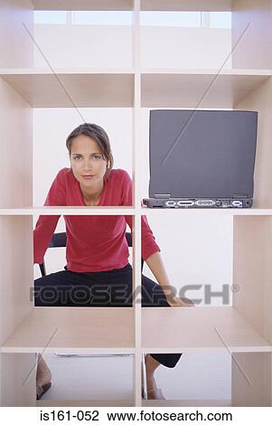 Stock Image - Woman sitting behind bookcase. Fotosearch