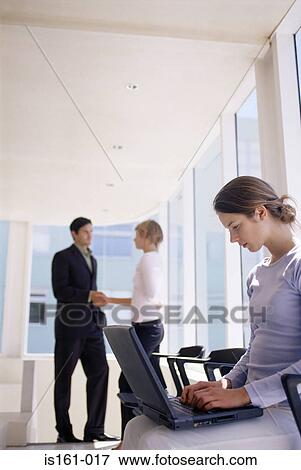 Stock Photo - Woman using laptop as colleagues shake hands. Fotosearch