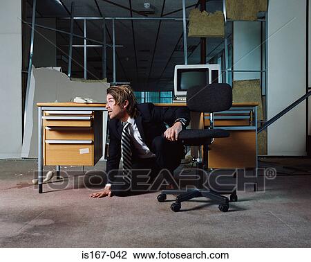 Stock Image - Businessman emerging from under desk. Fotosearch