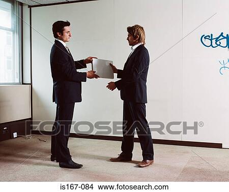 Picture - Businessmen exchanging a laptop computer. Fotosearch
