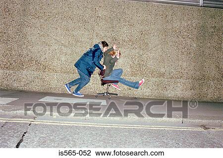 Stock Image - Couple playing on office chair. Fotosearch