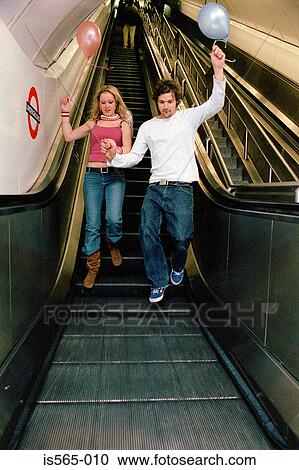 Stock Image - Couple with balloons on escalator. Fotosearch