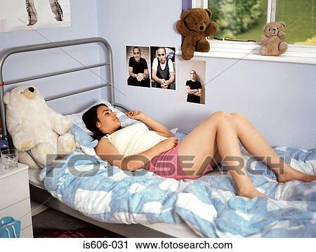 Stock Image - Girl smiling at posters in bedroom. Fotosearch
