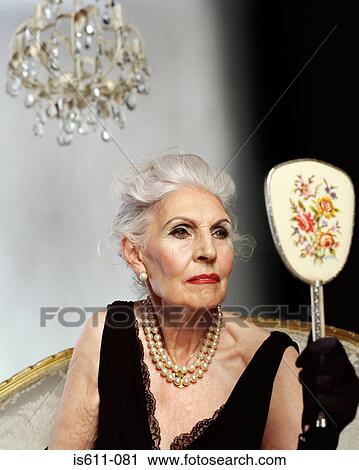 Glamorous senior woman looking at herself in hand mirror View Large Photo Image Stock Image - Glamorous senior woman looking at herself in hand mirror. Fotosearch