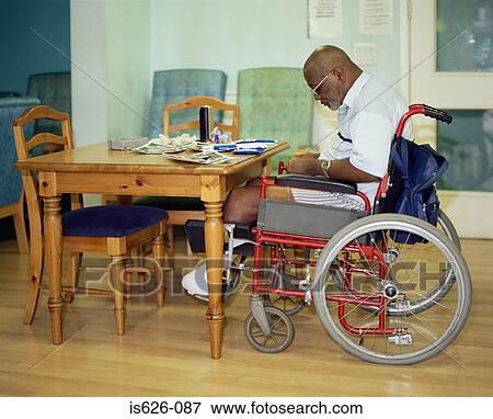 Stock Photo - Man in a wheelchair rolling a cigarette. Fotosearch