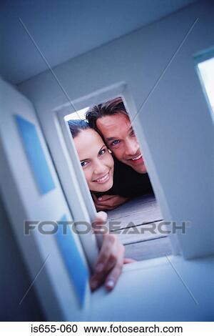 Stock Image - Couple looking through door of doll house. Fotosearch