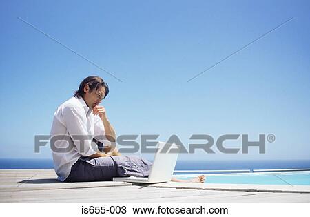 Stock Image - Man with laptop by swimming pool. Fotosearch
