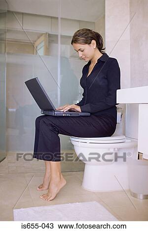 Stock Image - Woman sitting on a toilet using laptop computer. Fotosearch