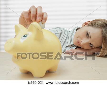Stock Image - Woman putting coin in piggy bank. Fotosearch