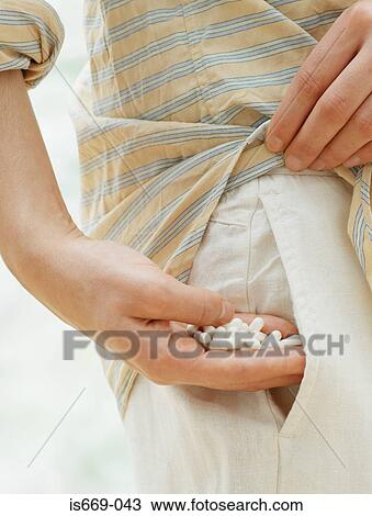 Stock Image - Woman taking handful of drugs from her pocket. Fotosearch