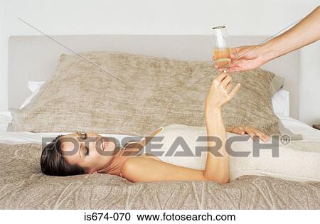 Stock Image - Woman lying on bed and taking champagne glass. Fotosearch
