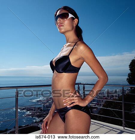 Stock Image - Woman standing on balcony in a bikini. Fotosearch