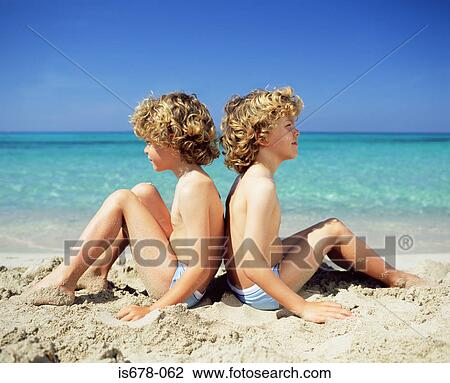 Stock Image - Twin boys sitting on the beach. Fotosearch