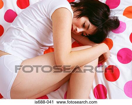 Stock Image - Woman curled up on bed. Fotosearch