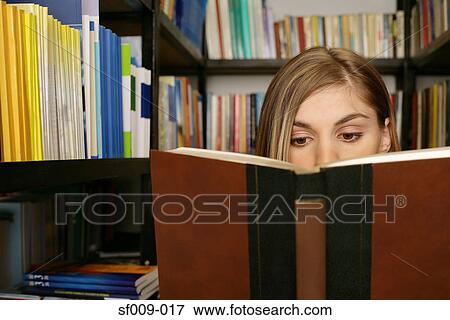 Young woman reading a book in library View Large Photo Image Stock Photo - Young woman reading a book in library. Fotosearch