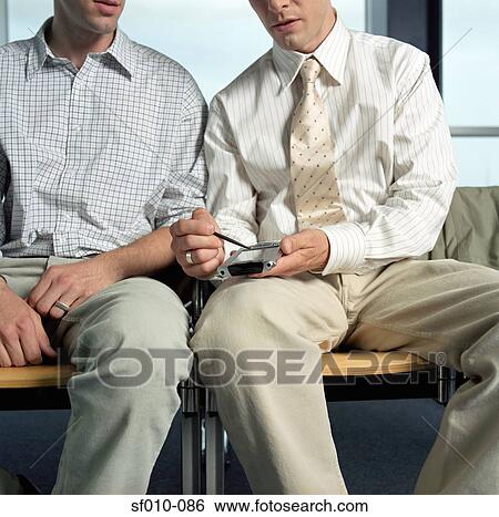 Stock Photograph - Businessmen looking at palmtop in departure lounge. Fotosearch