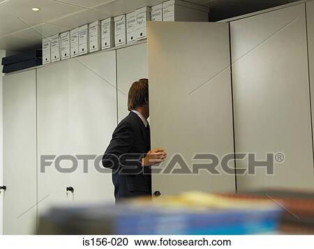 Stock Image - Office worker looking in cupboard. Fotosearch