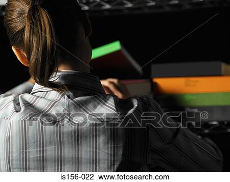 Stock Image - Office worker looking through a stack of books. Fotosearch