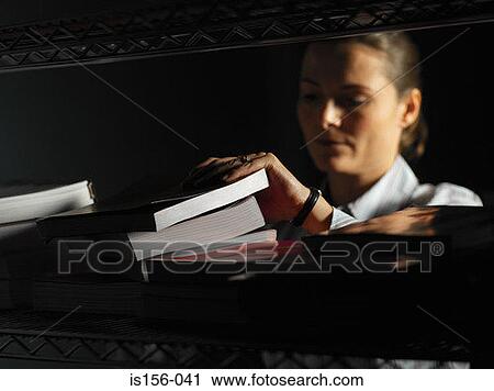 Stock Image - Office worker looking through a stack of books. Fotosearch