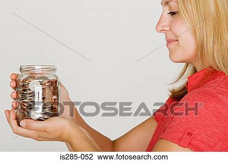 Stock Image - Woman holding jar of pennies. Fotosearch