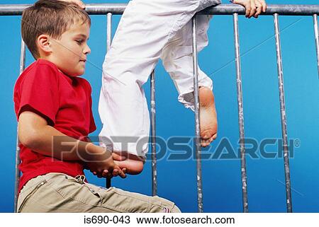 Stock Image - Boy helping friend onto a railing. Fotosearch