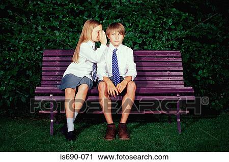 Girl whispering to boy on bench View Large Photo Image Stock Image - Girl whispering to boy on bench. Fotosearch