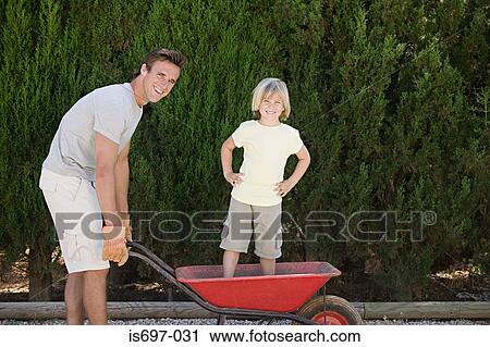Stock Image - Father pushing son in wheelbarrow. Fotosearch