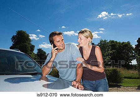Stock Image - Couple by car using mobile phone. Fotosearch