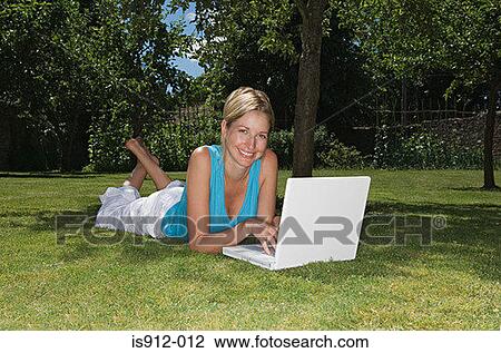 Stock Image - Woman lying on the grass using laptop . Fotosearch