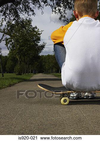 Stock Image - Boy sitting on a skateboard. Fotosearch