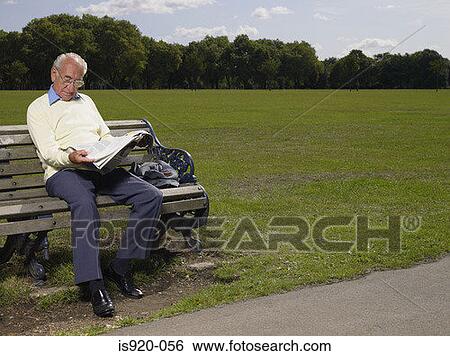 Stock Photograph - Elderly man reading a newspaper in a park. Fotosearch