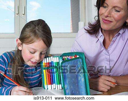 Stock Image - Mother watching daughter do homework. Fotosearch