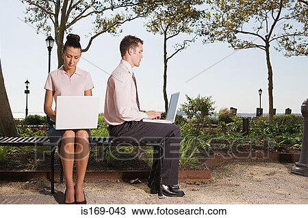 Stock Image - Two people telecommuting in a park. Fotosearch