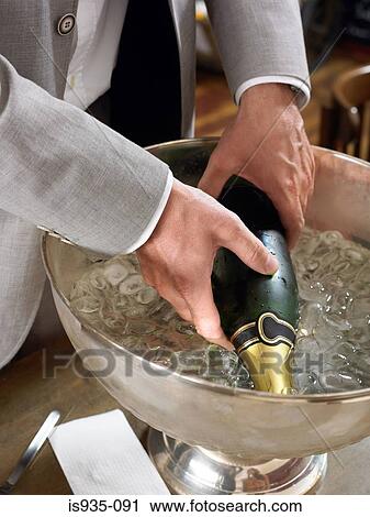 Stock Image - Man taking champagne bottle from ice bucket. Fotosearch