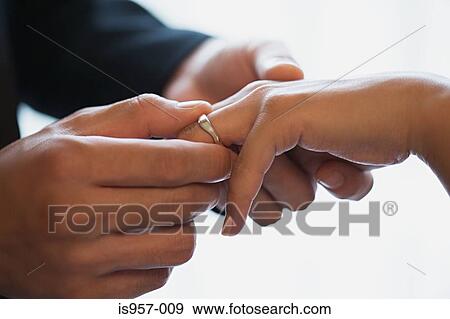 Stock Photo - Groom placing wedding ring on brides finger. Fotosearch