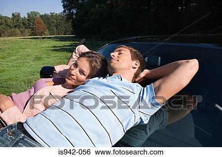 Stock Photograph - Couple relaxing on car hood. Fotosearch