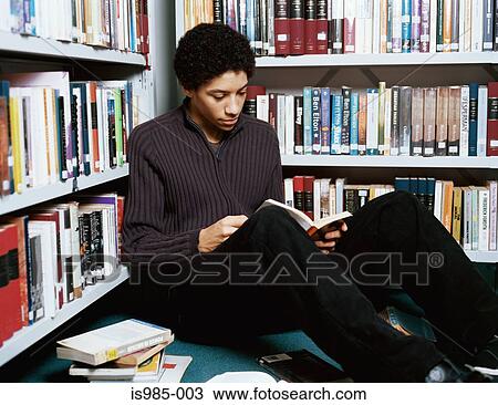 Stock Image - Teenage boy reading in library. Fotosearch