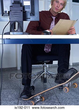 Man with skateboard under his desk View Large Photo Image Stock Image - Man with skateboard under his desk. Fotosearch